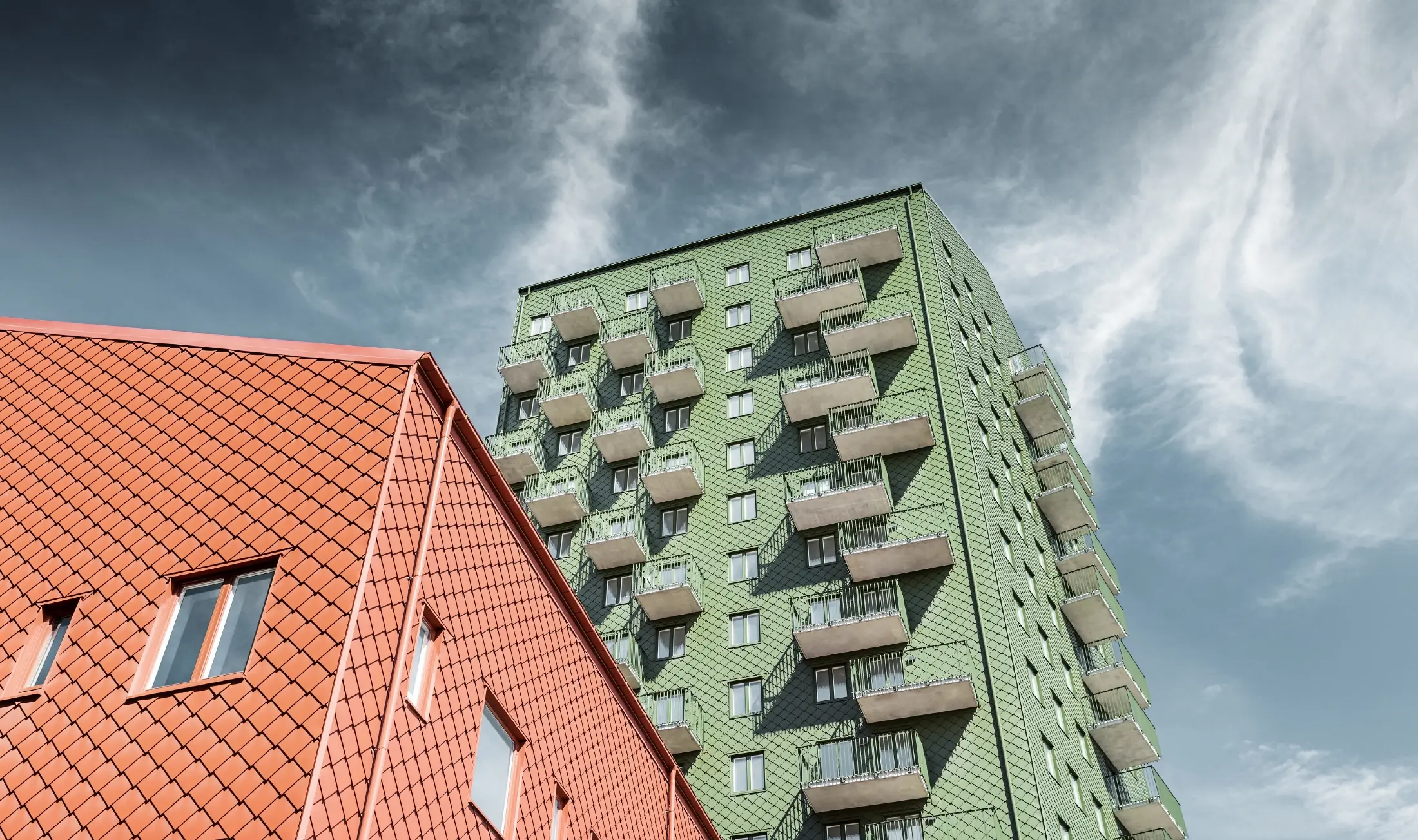 Flatgebouwen met balkons die bekleed zijn met PREFA gevellosange 29 × 29 in olijfgroen en baksteenrood