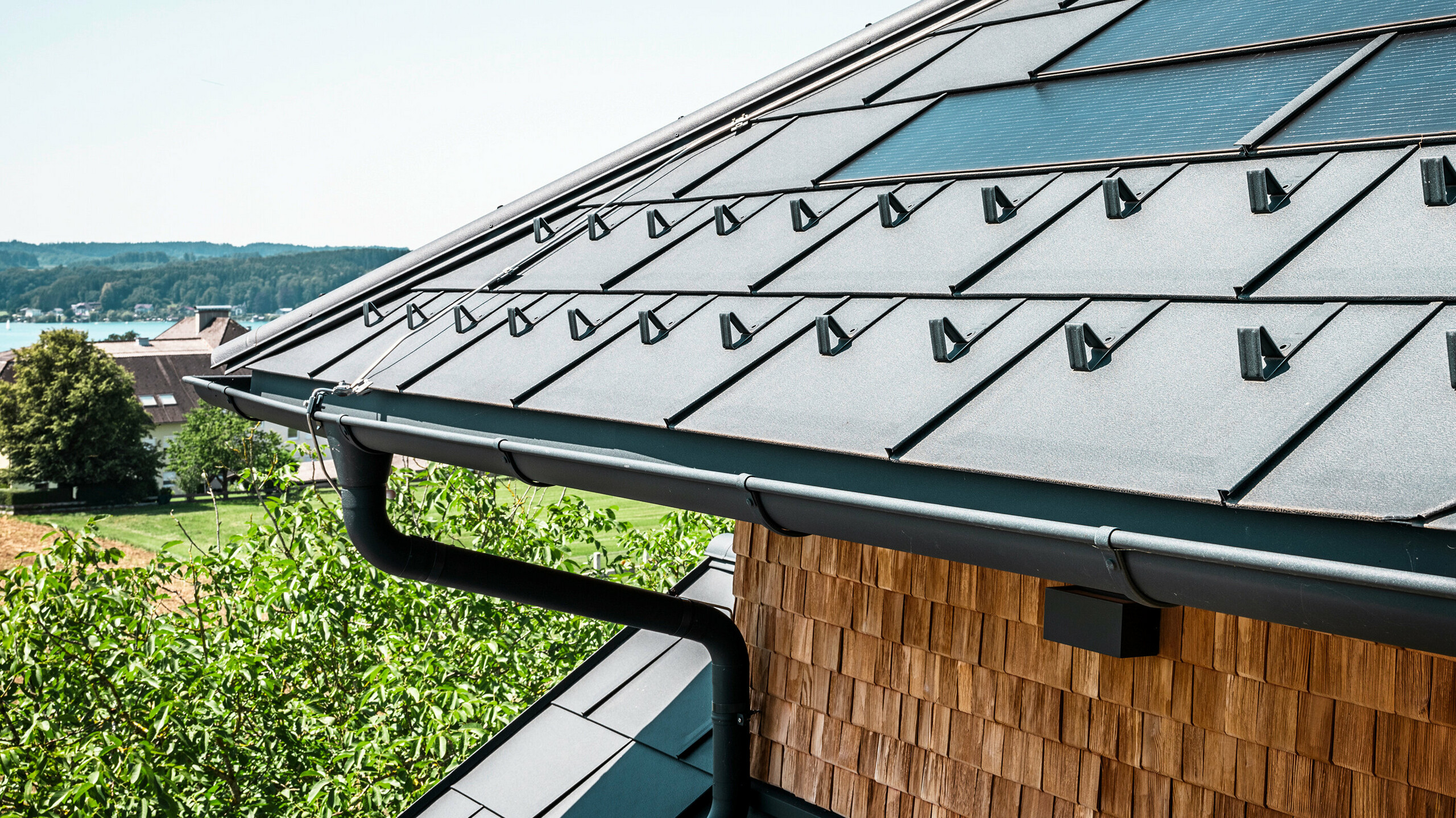 De Zenz'n Stub'n in Schörfling aan de Attersee heeft een nieuw gerenoveerd dak met innovatieve PREFA solar-dakpan en duurzame PREFA dakpan R.16 in P.10 antraciet. Het stijlvolle aluminium dak combineert modern design met duurzame energieopwekking. Ook de dakafvoersystemen, bestaande uit afvoerbuizen en mastgoten in P.10 antraciet, passen harmonieus in het totaalbeeld en onderstrepen de hoogwaardige afwerking. Op de achtergrond schittert het blauw van de Attersee.