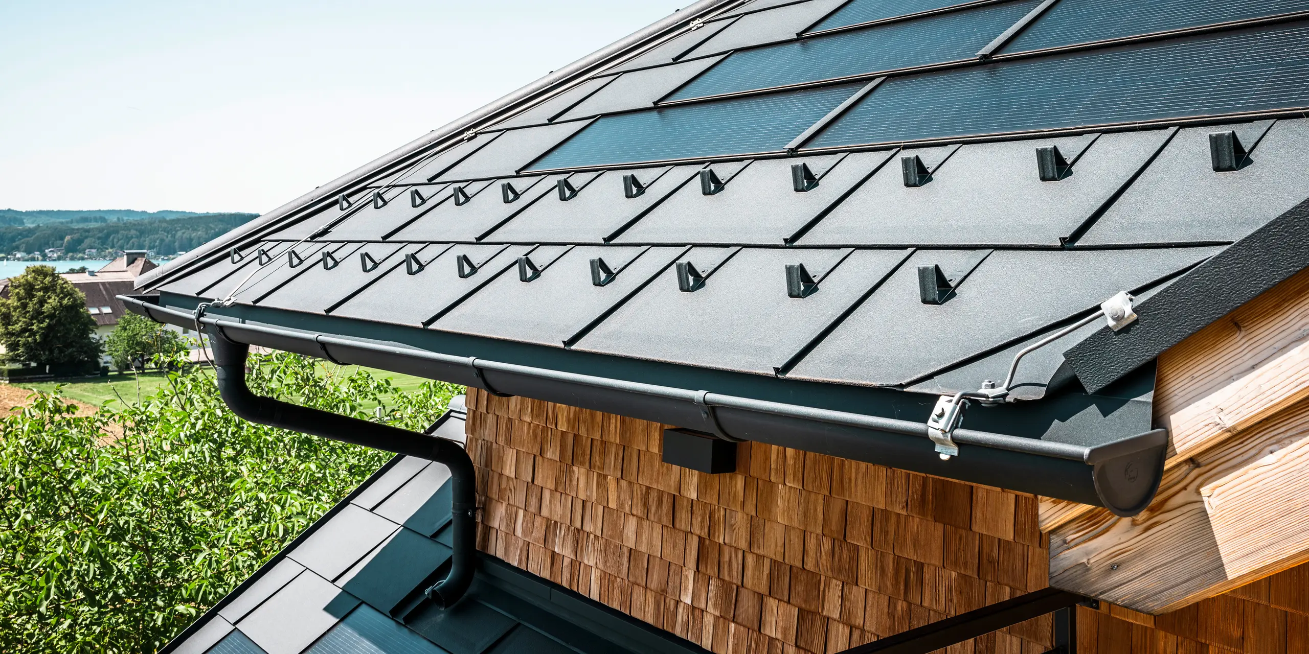 De Zenz'n Stub'n in Schörfling aan de Attersee heeft een nieuw gerenoveerd dak met innovatieve PREFA solar-dakpan en duurzame PREFA dakpan R.16 in P.10 antraciet. Het stijlvolle aluminium dak combineert modern design met duurzame energieopwekking. Ook de dakafvoersystemen, bestaande uit afvoerbuizen en mastgoten in P.10 antraciet, passen harmonieus in het totaalbeeld en onderstrepen de hoogwaardige afwerking. Op de achtergrond schittert het blauw van de Attersee.