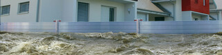 Auf dem Bild ist ein PREFA Hochwasserschutz zu sehen, der mehrere Häuser von großen Wassermengen schützt.