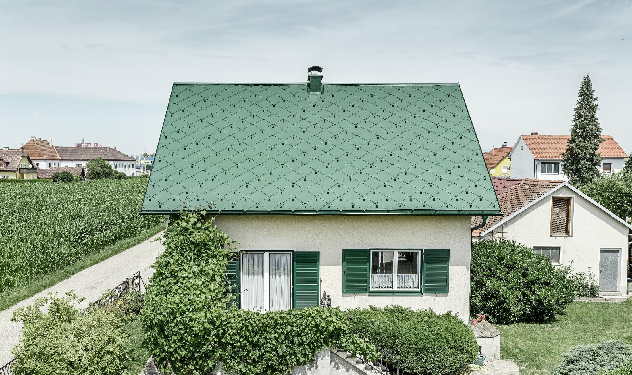 Klassieke eengezinswoning met zadeldak met een dakbedekking van aluminium in mosgroen met groene luiken. Het dak is bedekt met PREFA daklosanges van 44 × 44 in P.10 mosgroen.
