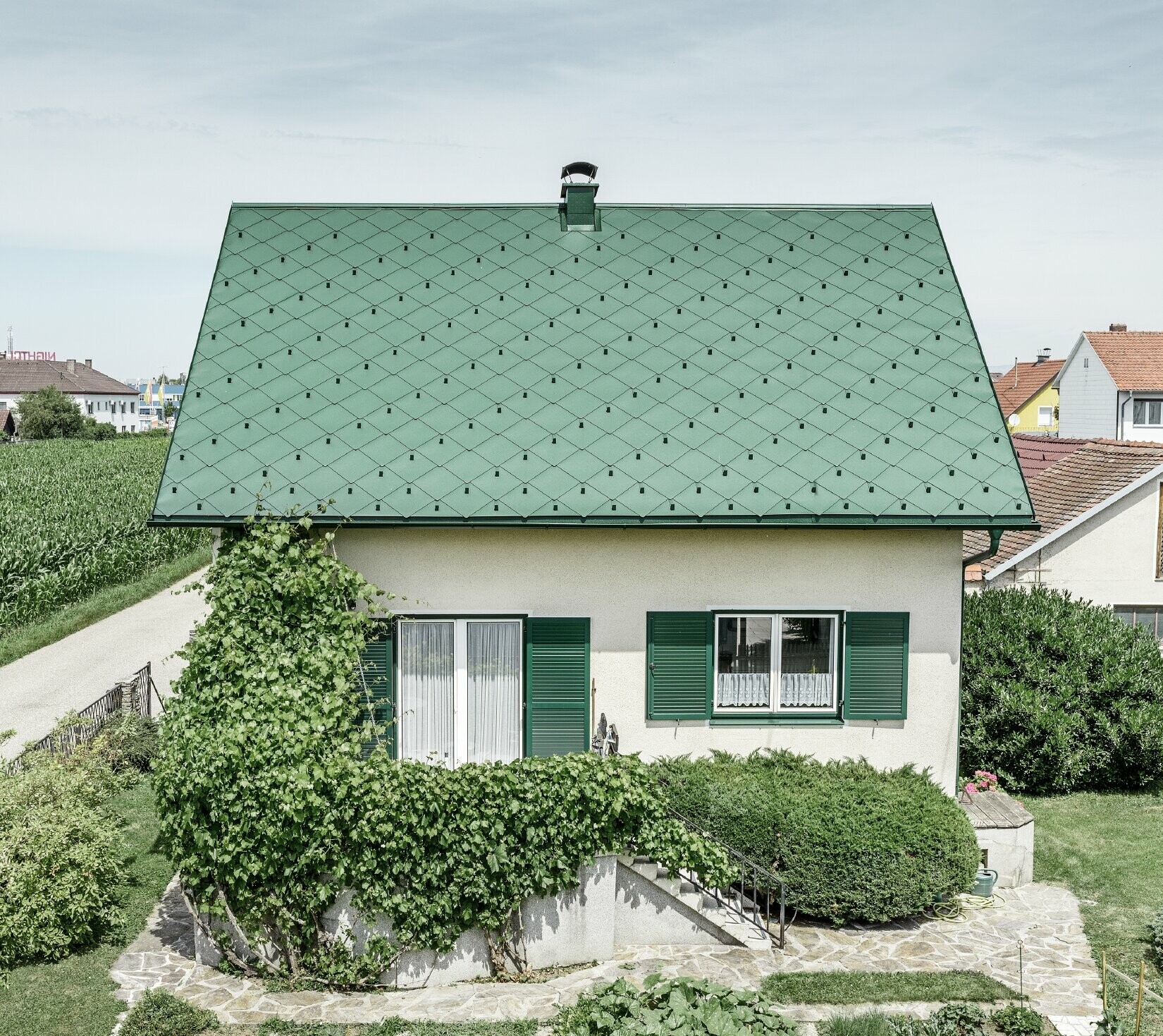 Klassieke eengezinswoning met zadeldak met een dakbedekking van aluminium in mosgroen met groene luiken. Het dak is bedekt met PREFA daklosanges van 44 × 44 in P.10 mosgroen.