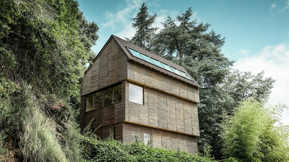Ein Haus im Westen Frankreichs mit PREFA-Dachschindeln in der Farbe P.10 Walnussbraun, gelegen an einem steilen Hang – ein modernes Design mit einer Fassade aus Weidenholz und einem energieeffizienten Dach.