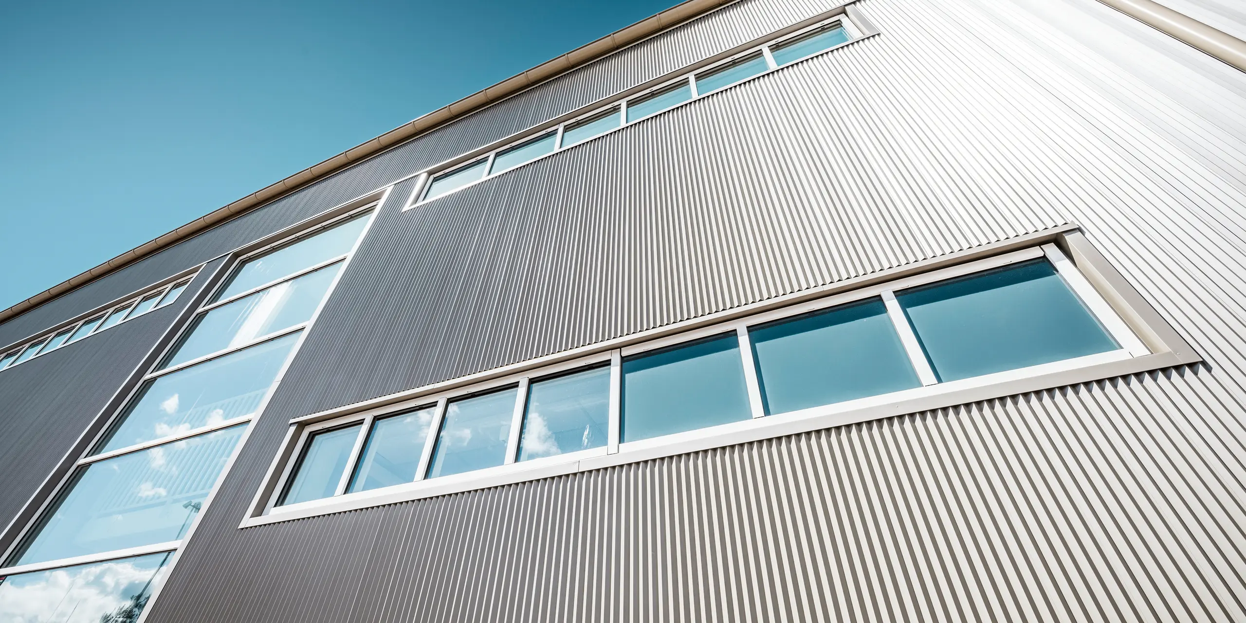 Buitenkant van de Park Arena in Värnamo, Zweden, met een moderne PREFA gevel in brons. De kartelprofielen van aluminium zorgen voor opvallende licht- en schaduweffecten. De ingebouwde ramen passen harmonieus in de nauwkeurig afgewerkte gevel, die staat voor duurzaamheid, weerstand en een eigentijds design.