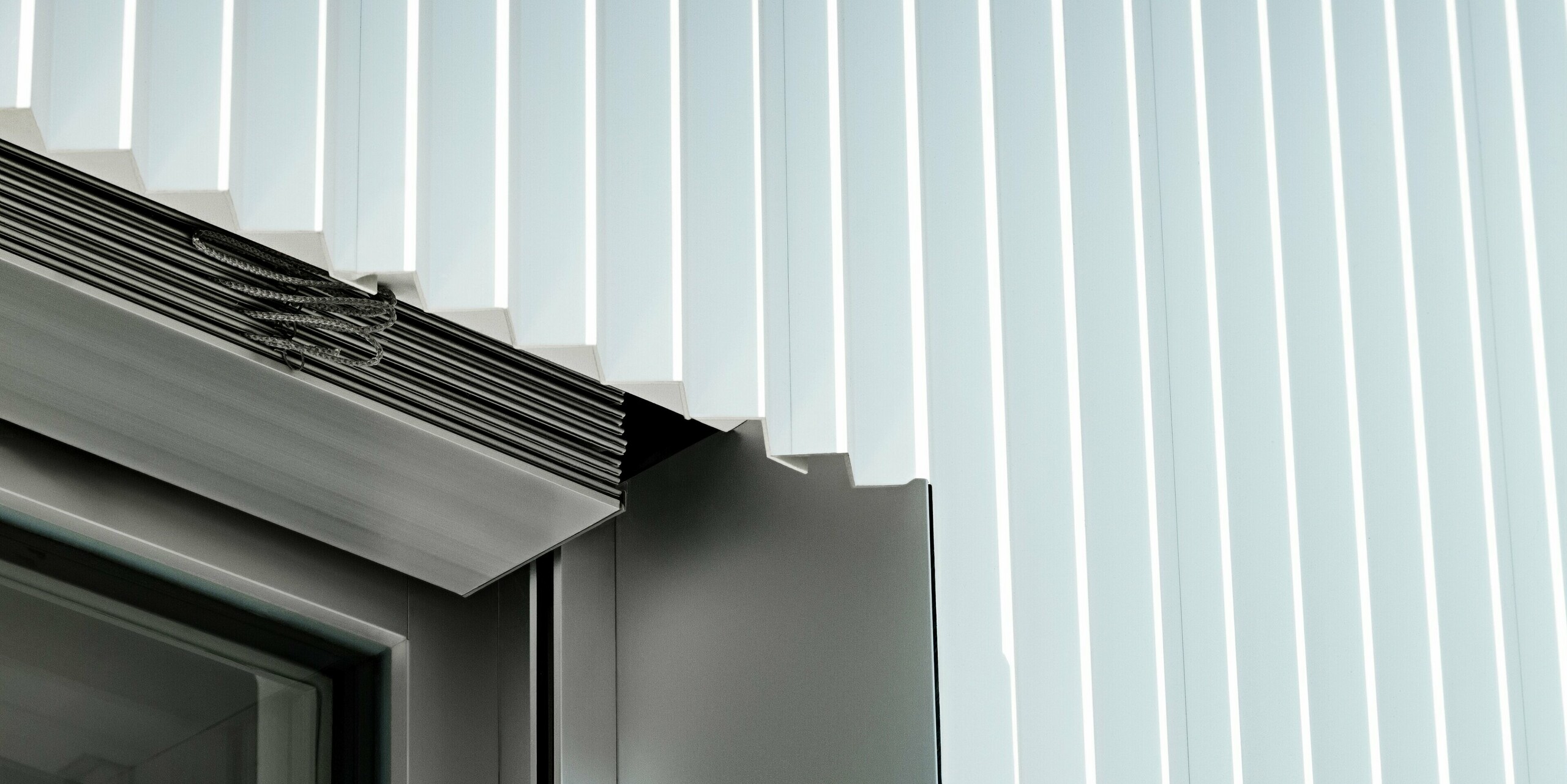 Präzise Detailaufnahme einer Fensterlaibung mit PREFA Zackenprofil in P.10 Reinweiß. Die klar geformten Aluminiumprofile treffen exakt auf das Fenster, das mit integrierter Raffstoreführung ergänzt ist. Die hochwertige Ausführung zeigt die perfekte Verarbeitung, Langlebigkeit und Witterungsbeständigkeit der PREFA Fassadensysteme – ideal für moderne Architektur mit Anspruch.