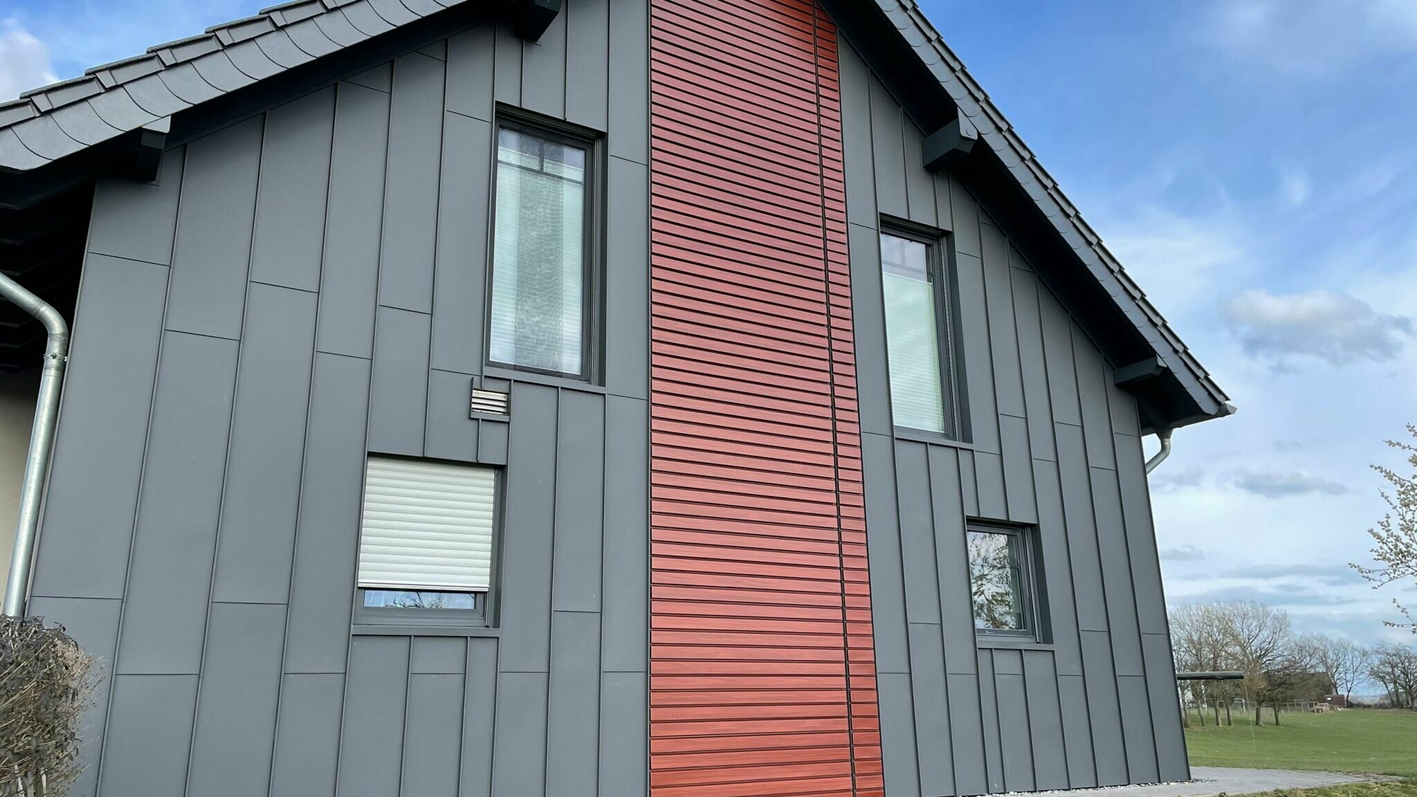 Fassadengestaltung einer renovierten Fassade mit PREFA Prefalz, vertikal verlegt in mehreren Farben, Dunkelgrau und Rot