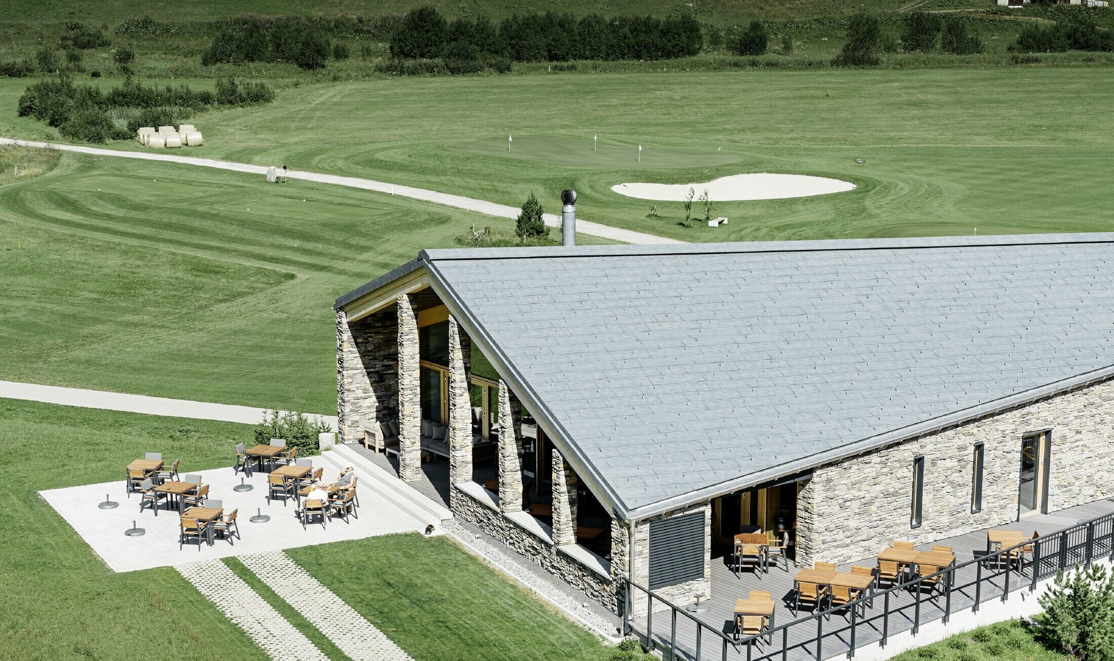 Modern clubhuis van golfterrein in Andermatt (Zwitserland) met gevel in natuursteen en aluminium FX.12 dakpanelen in steengrijs van PREFA 