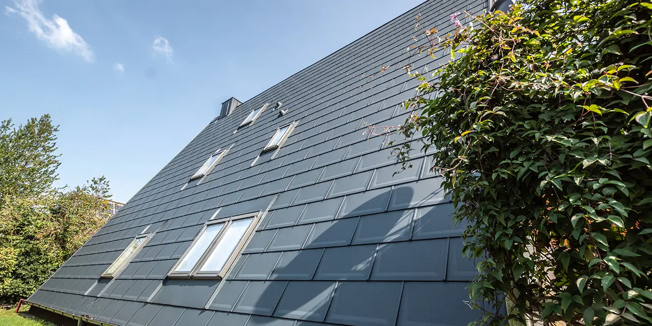 Lang dakvlak van een A-framewoning gedekt met de PREFA dakpan in P.10 antraciet. In het dakvlak zijn een aantal dakramen geplaatst.