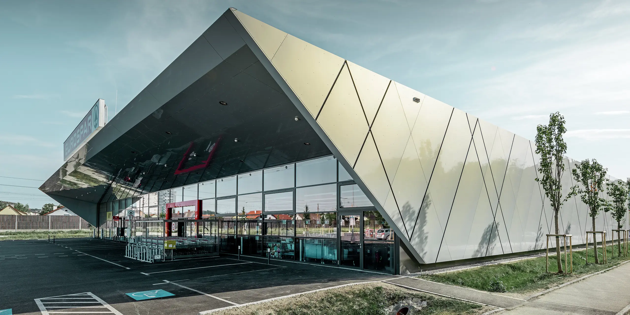 Entreegedeelte van het nieuwe Eurospar filiaal in Wels met het moderne gevelpaneel van PREFA in zilver goud; afhankelijk van de kijkhoek glinsteren de aluminium composietplaten in de zon in verschillende kleuren.
