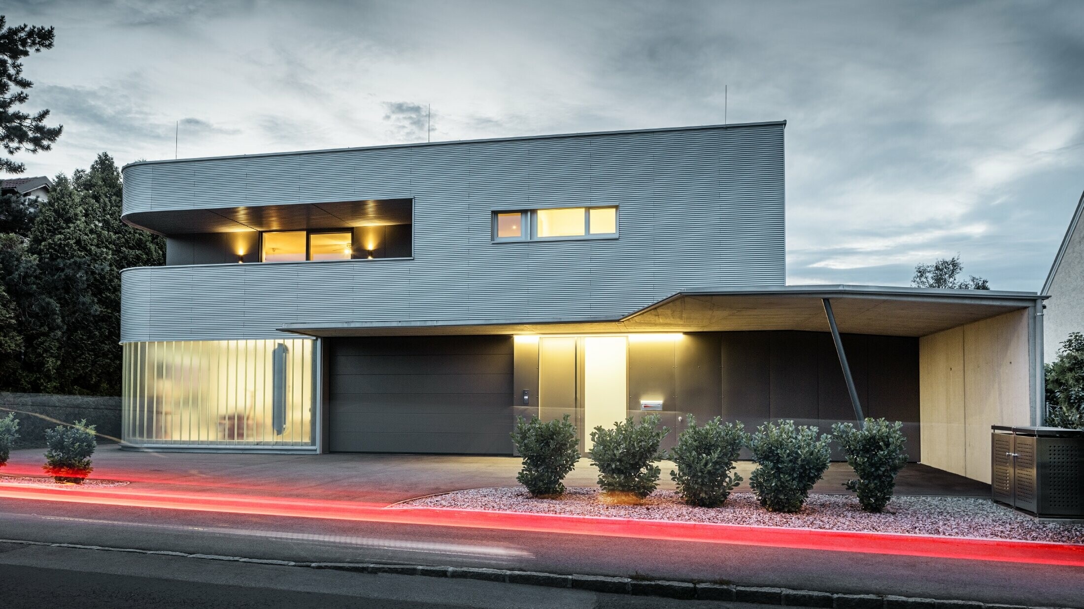 Modern woongebouw met PREFA golfplaatgevel in blank naturel met garage, gefotografeerd bij avondlicht