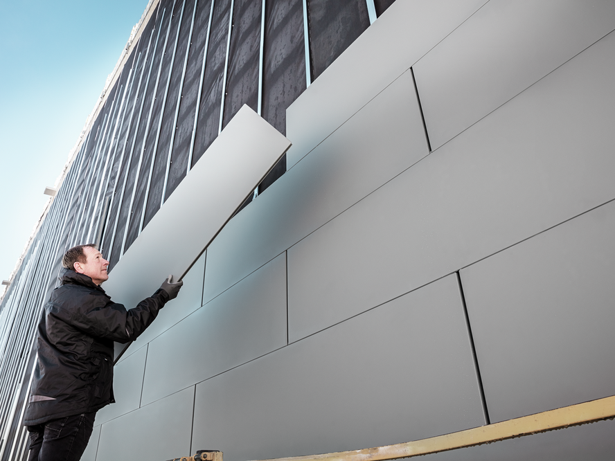 Ein Handwerker deckt eine Fassade mit Sidings ein.