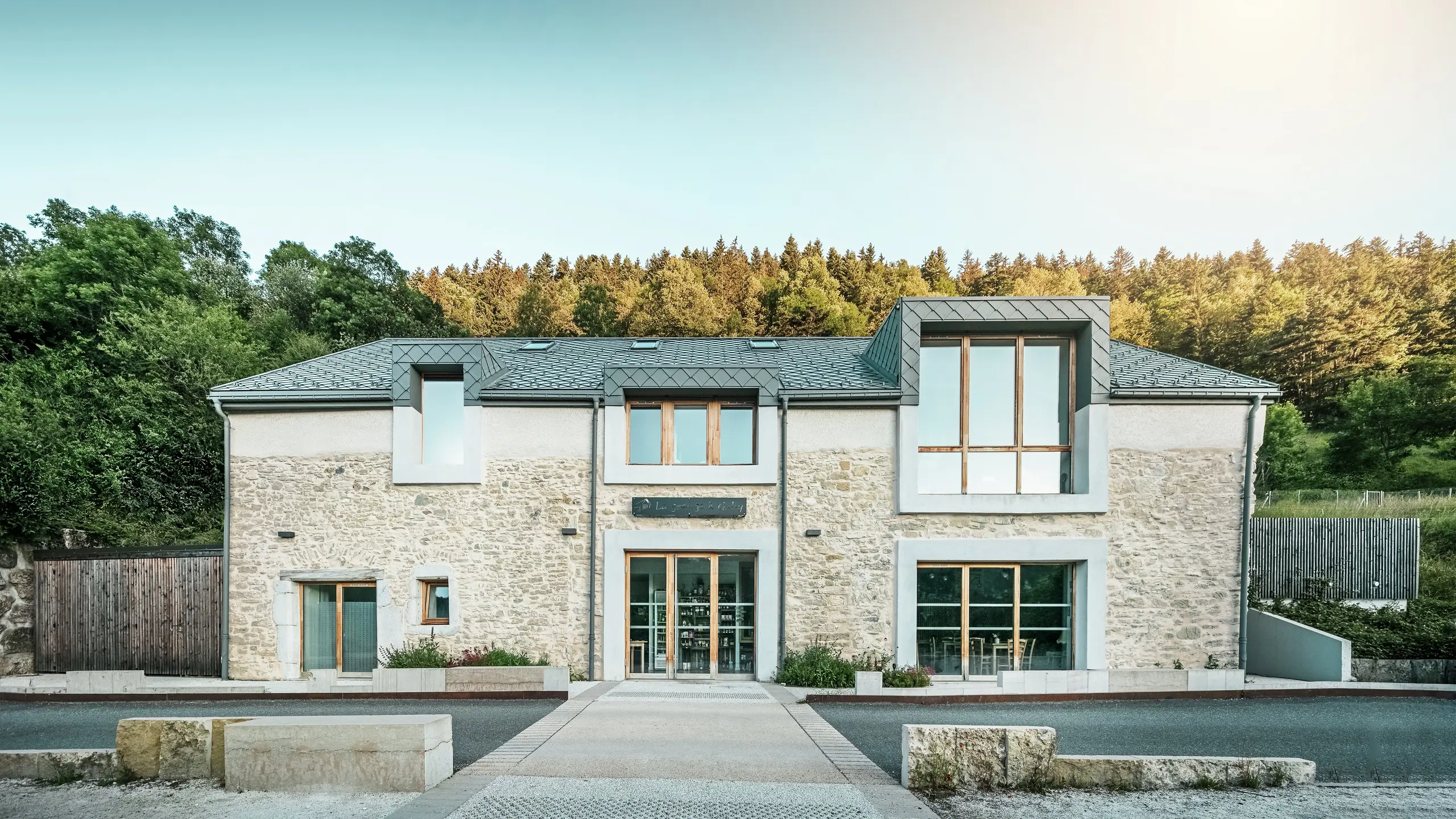 Vorderansicht der renovierten Scheune „La Grange à Gaby“ in Engins, Frankreich. Die Kombination aus traditionellem Steinmauerwerk und einem modernen PREFA-Aluminiumdach mit 29 × 29 cm großen Rauten verleiht dem Gebäude ein harmonisches und zeitgemäßes Erscheinungsbild. Heute dient die Scheune als kultureller Treffpunkt und als Übernachtungsmöglichkeit.