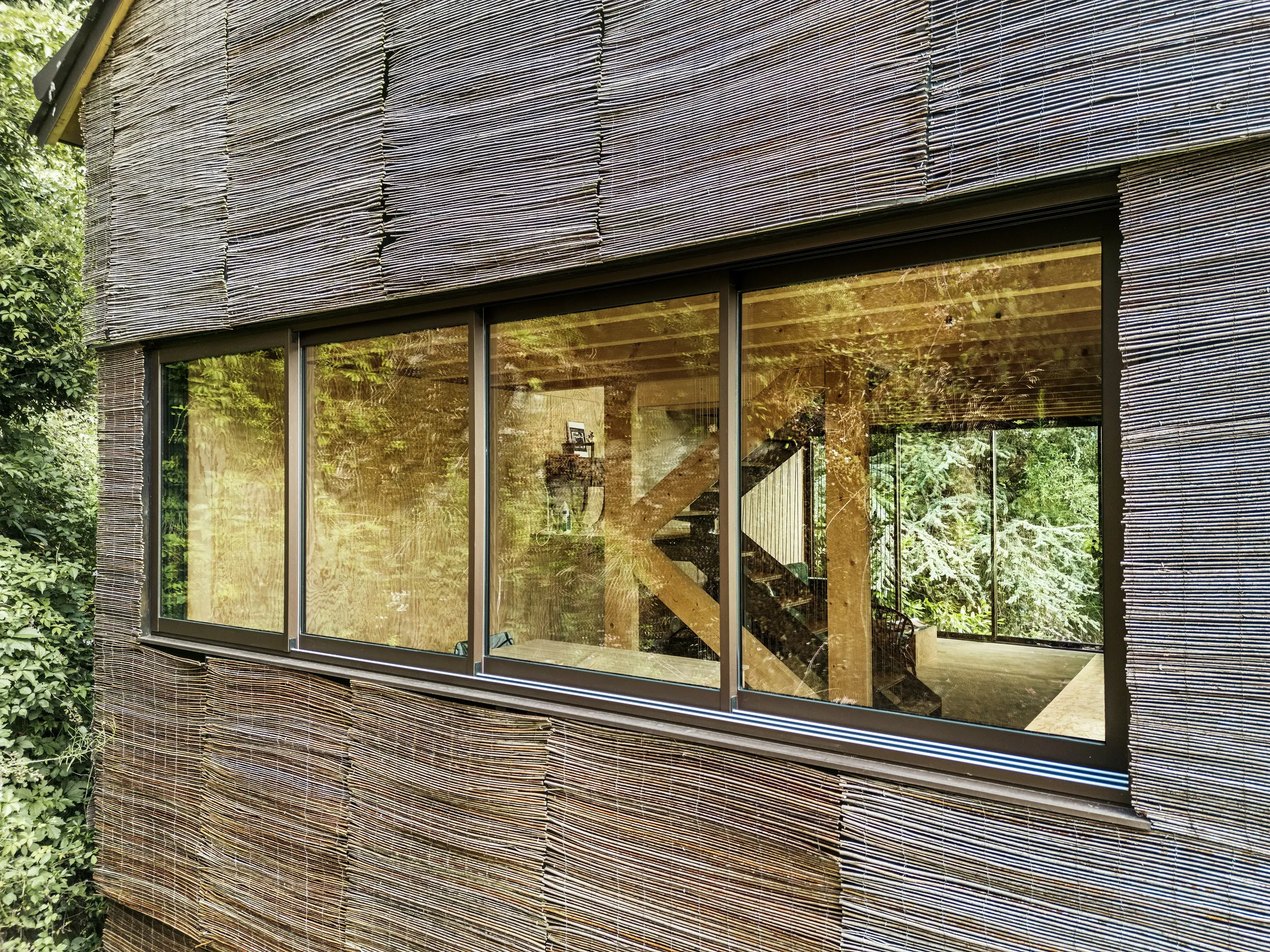 Detail eines modernen Aluminiumrahmenfensters mit Weidenholzfassade an einem Haus in Frankreich – nachhaltiges Design mit PREFA-Dachschindeln und natürlicher Umgebung.