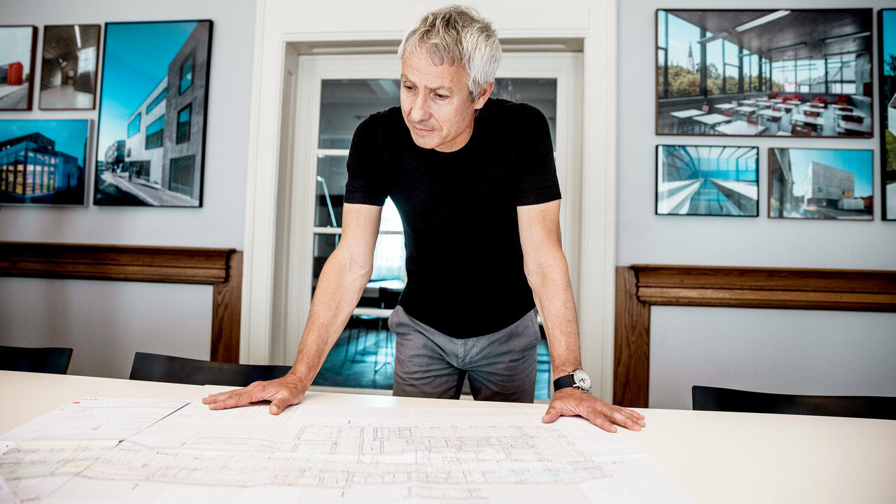 Een architect werkt aan gedetailleerde bouwtekeningen in een modern kantoor, omringd door indrukwekkende foto’s van PREFA-architectuurprojecten.