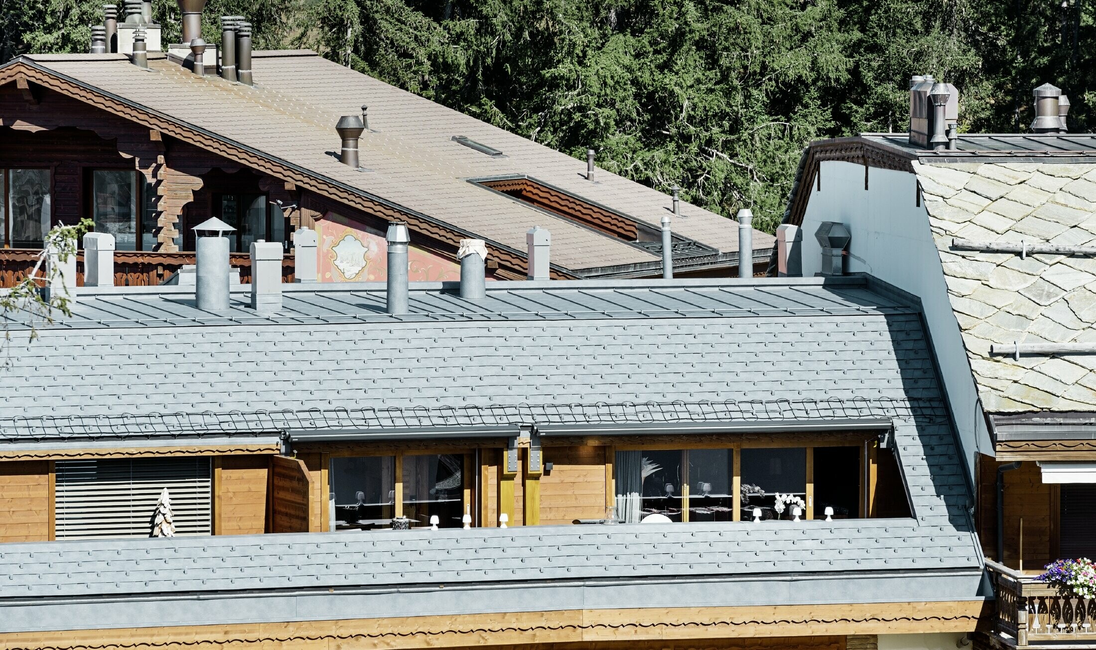 Meergezinswoning in Crans Montana (Zwitserland) met de bergen als decor, een gevel met speelse houten elementen en een dakbedekking bestaande uit aluminium PREFA-dakschindels in steengrijs