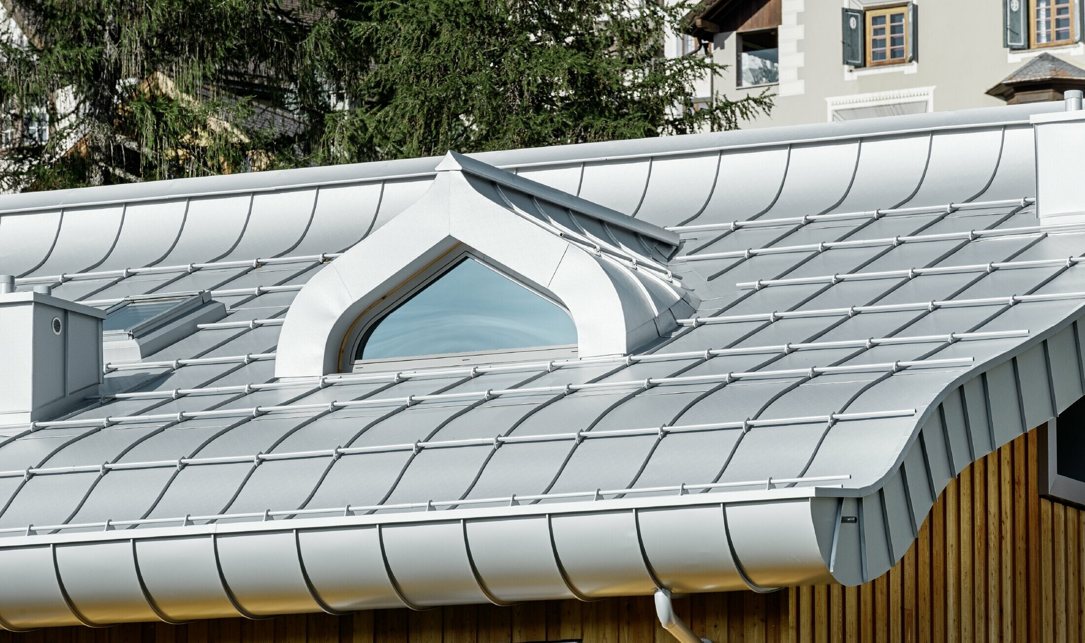 Meergezinswoning in Sankt Moritz (Zwitserland) met houten gevel en aluminiumdak met gekromde dakrand in zilver metallic