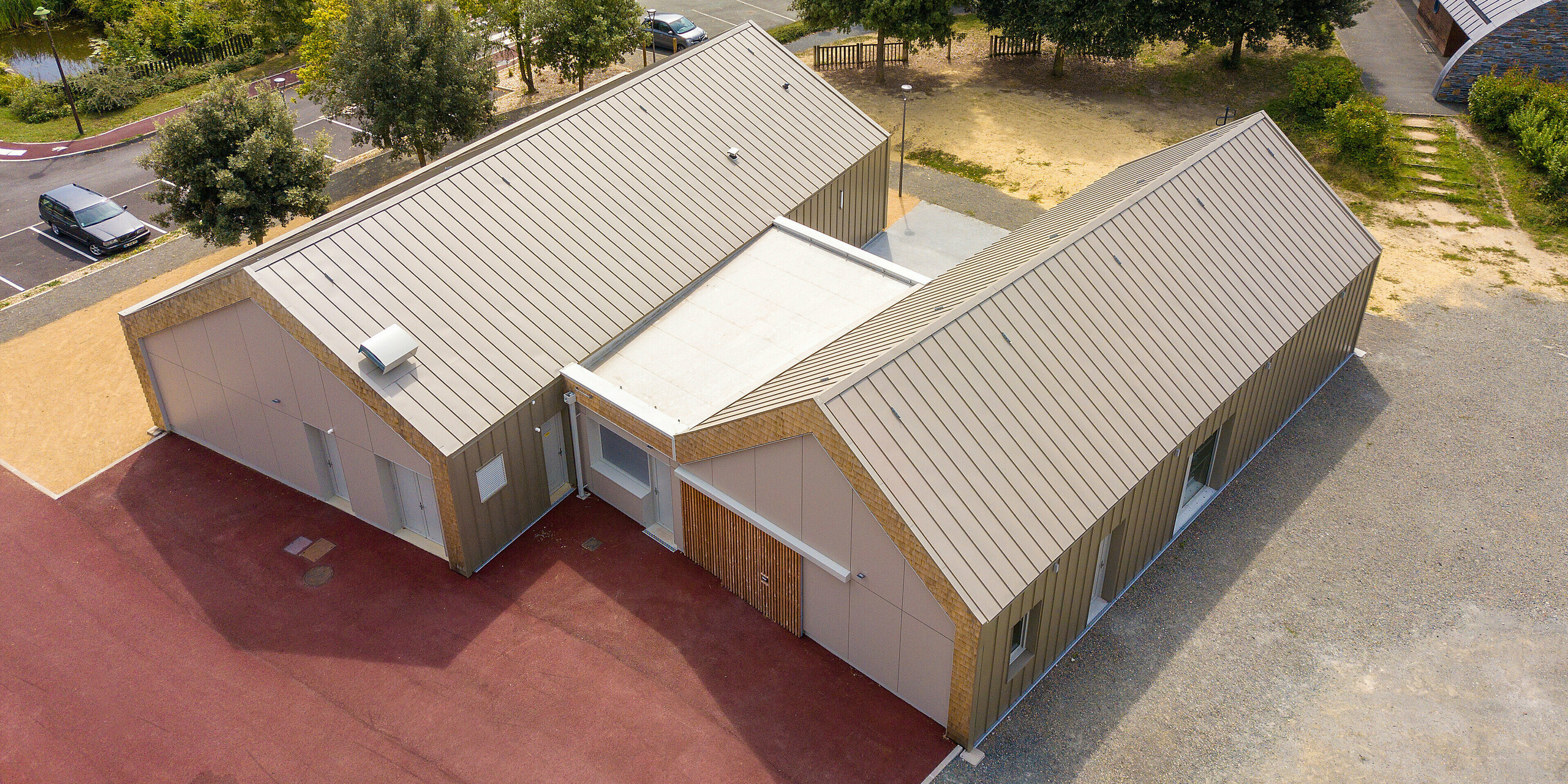 Vogelperspektive auf das Jugendzentrum Salles Espace Bellevue in Mûrs-Erigné, Frankreich. Beide Gebäude sind mit einer Stehfalzverkleidung aus PREFALZ in Bronze ausgestattet. Die witterungsbeständige und langlebige Aluminiumbekleidung von PREFA bietet eine moderne und nachhaltige Lösung für architektonisch anspruchsvolle Projekte.