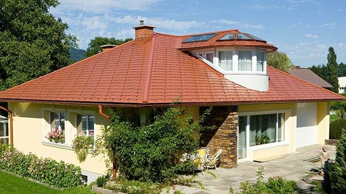 Eengezinswoning met schilddak en dakkapel bedekt met de aluminium PREFA-dakschindel in dakpanlook, baksteenrood.