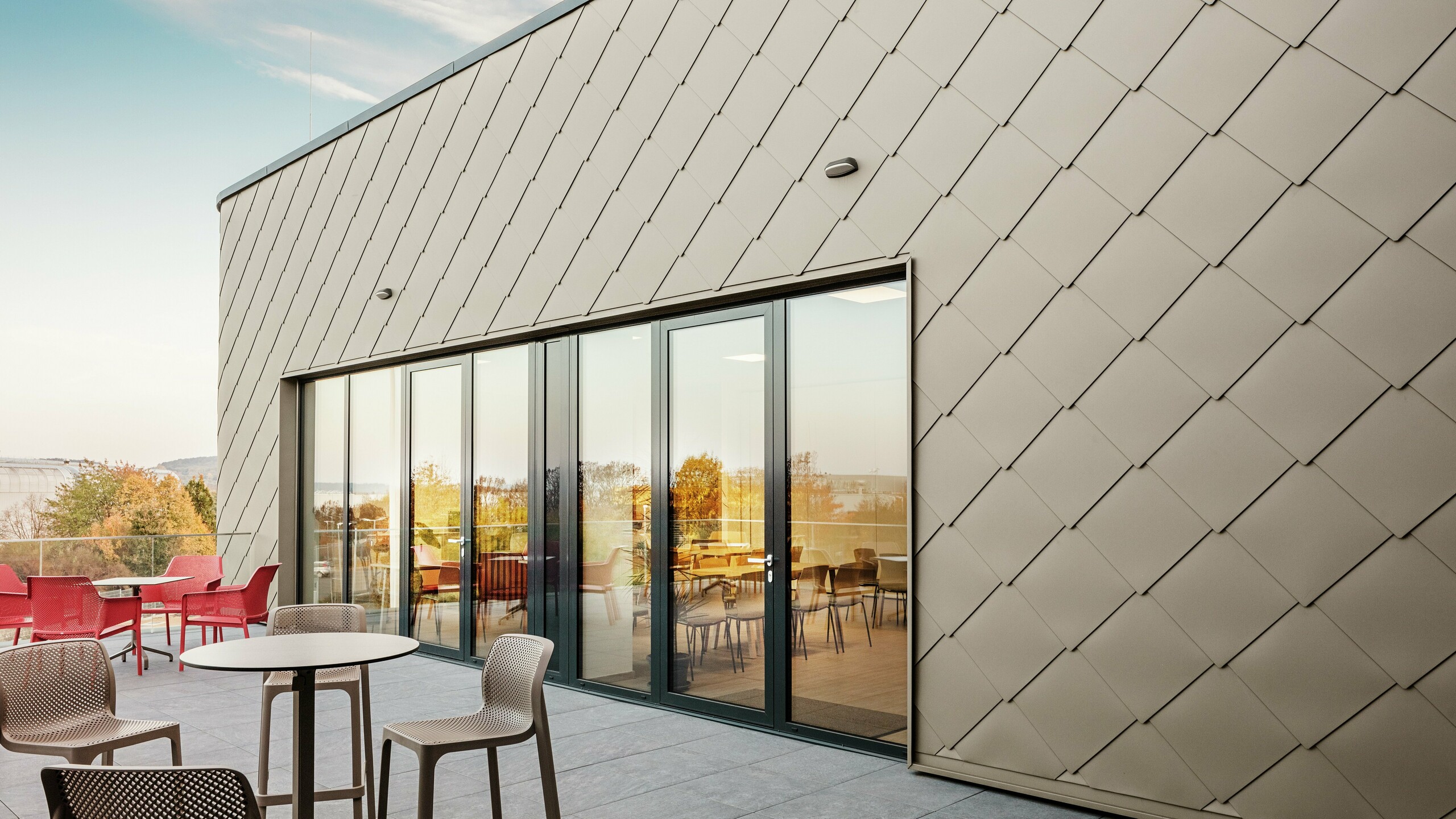Die Fassade des neuen PREFA Standortes in Törökbálint besticht durch die eleganten PREFA Wandrauten 44 × 44 in P.10 Prefabronze. Die präzise verlegte Aluminiumfassade sorgt für ein modernes, dynamisches Erscheinungsbild und bietet gleichzeitig maximalen Schutz vor Witterungseinflüssen. Die großzügige Glasfront verbindet Innen- und Außenbereich und schafft auf der großzügigen Terrasse eine helle und einladende Atmosphäre.