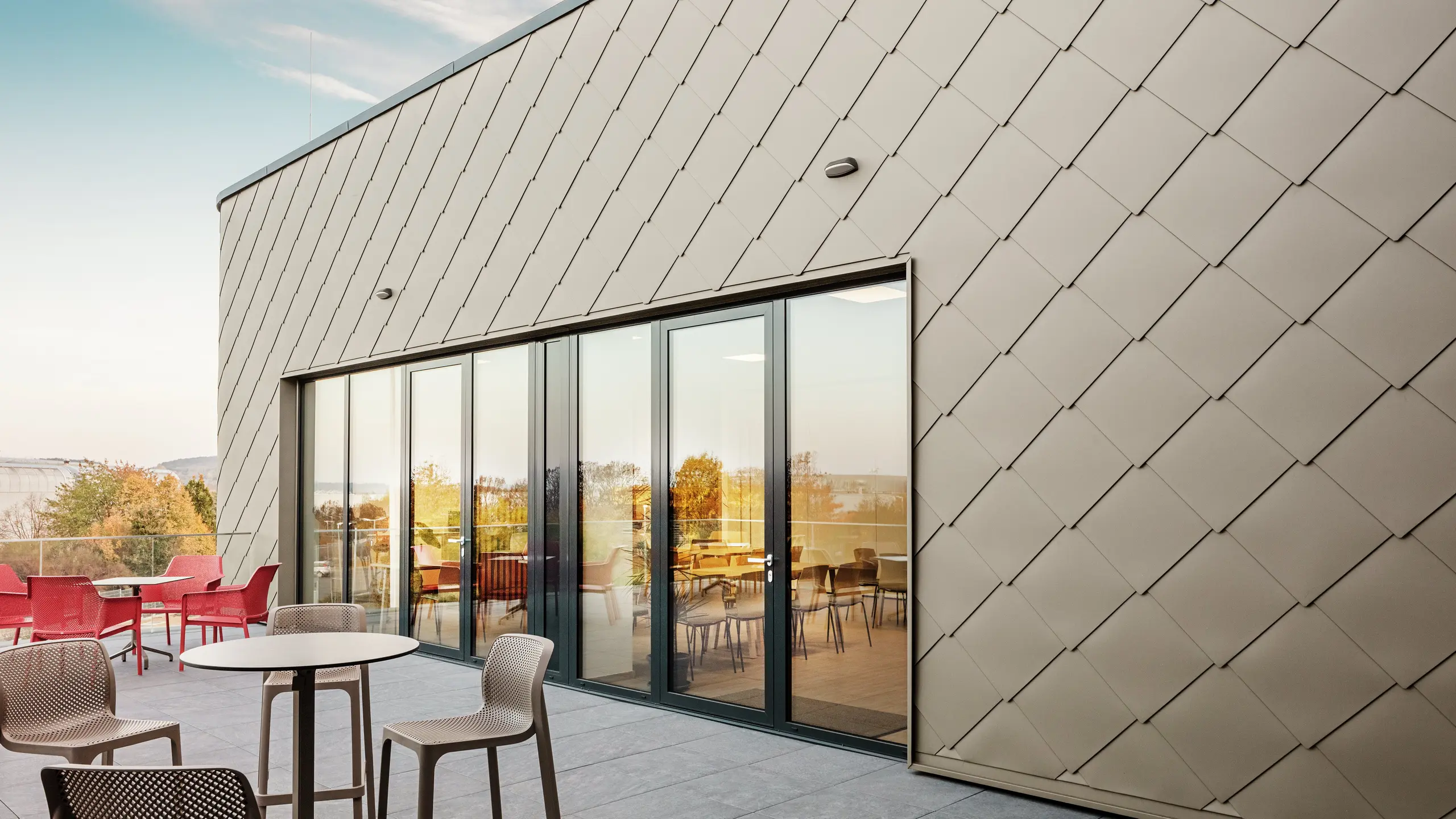 Die Fassade des neuen PREFA Standortes in Törökbálint besticht durch die eleganten PREFA Wandrauten 44 × 44 in P.10 Prefabronze. Die präzise verlegte Aluminiumfassade sorgt für ein modernes, dynamisches Erscheinungsbild und bietet gleichzeitig maximalen Schutz vor Witterungseinflüssen. Die großzügige Glasfront verbindet Innen- und Außenbereich und schafft auf der großzügigen Terrasse eine helle und einladende Atmosphäre.
