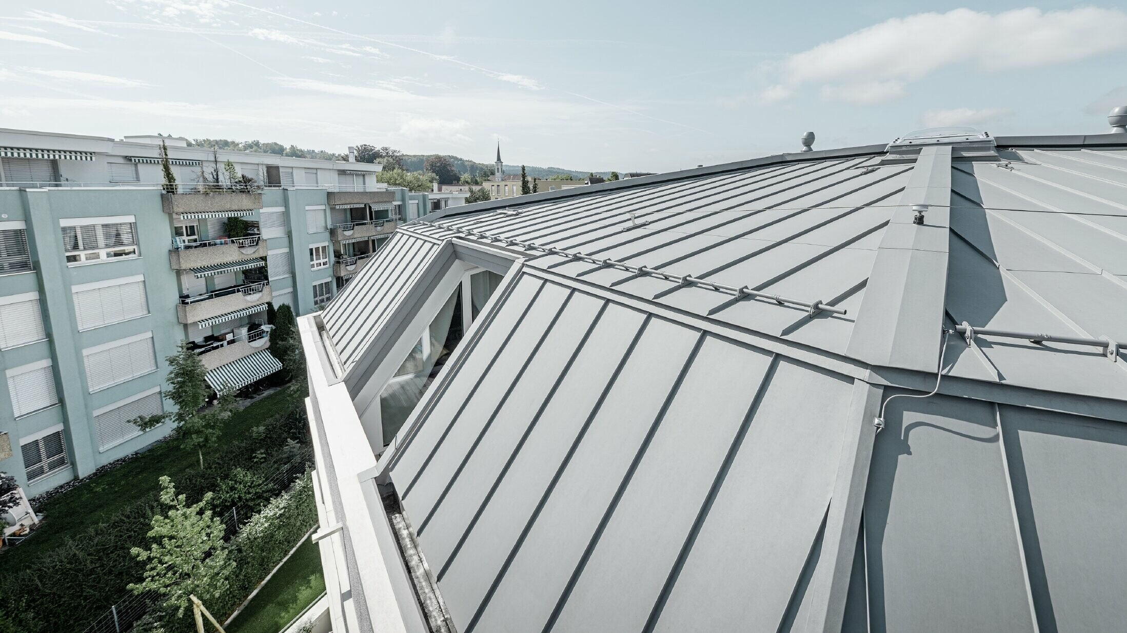 Detailbeeld van het dakvlak van een woongebouw; staand felsdak uitgevoerd in PREFA Prefalz in patinagrijs.