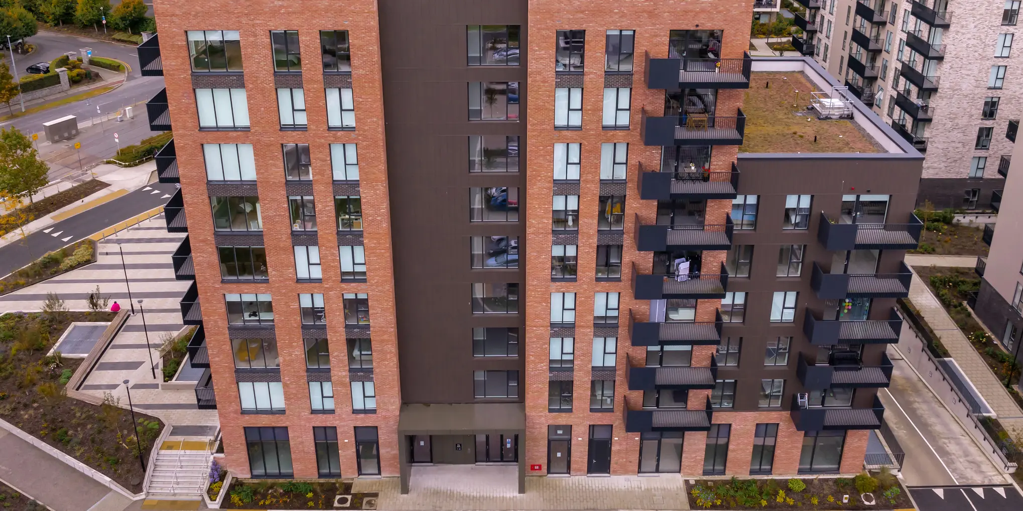 Die Citywest Apartments in Dublin aus der Vogelperspektive. Die Fassadenkombination aus traditionellem Backstein und 700 m² PREFA Sidings in P.10 Braun fügt sich harmonisch in die moderne Architektur und Umgebung ein.  Zu sehen ist der Eingangsbereich der Wohnanlage mit gepflegten Grünflächen rund um das Gebäude.