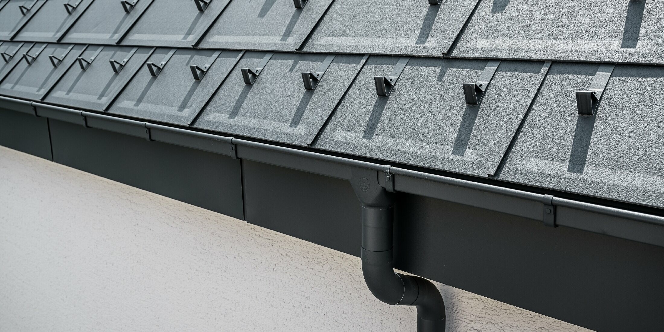 Steil dakoppervlak bedekt met de dakpan R.16 met vierkante PREFA bakgoot met trechteruitloop en afvoerbuis in antraciet