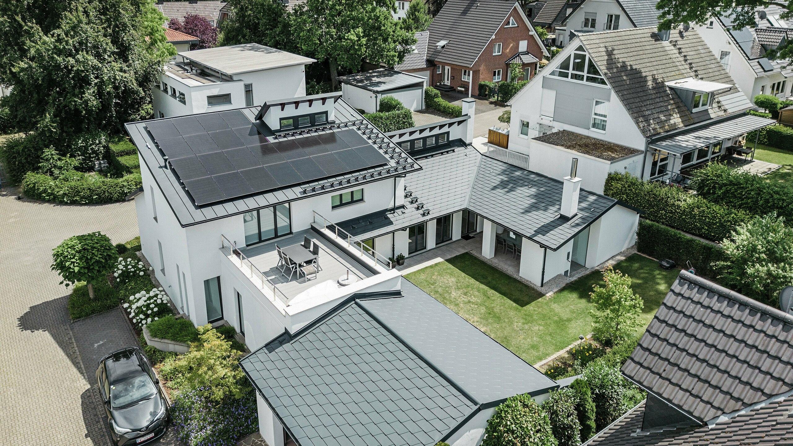 Uitzicht in vogelvlucht op het markante daklandschap van een eengezinswoning in Dortmund met PREFA dakshingles DS.19 en PREFALZ in P.10 antraciet en een grootschalige PV-installatie