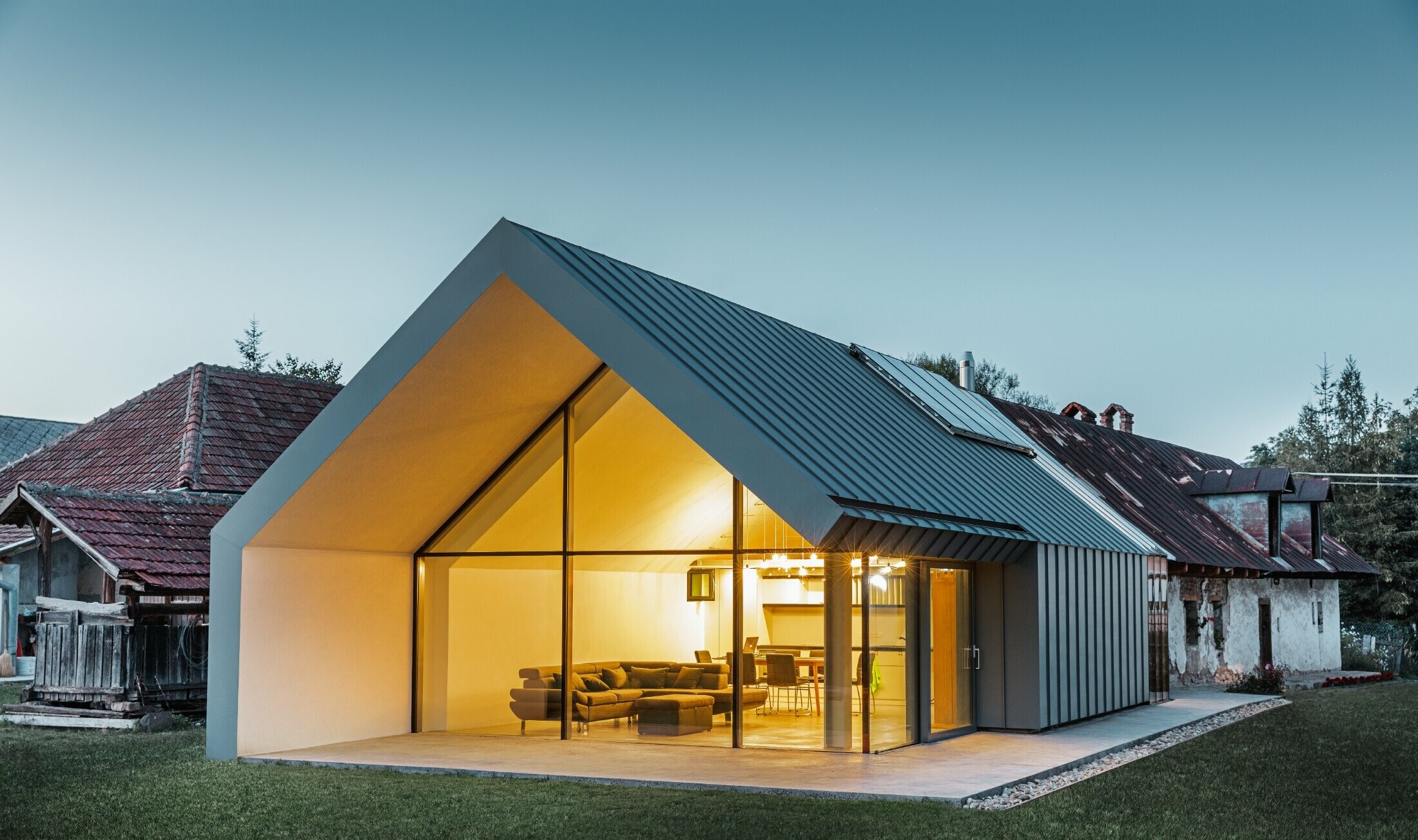 Modern architectenbureau/woning gebouwd tegen een oude boerderij, bekleed met staande naden en gebogen staande naden van PREFA in lichtgrijs