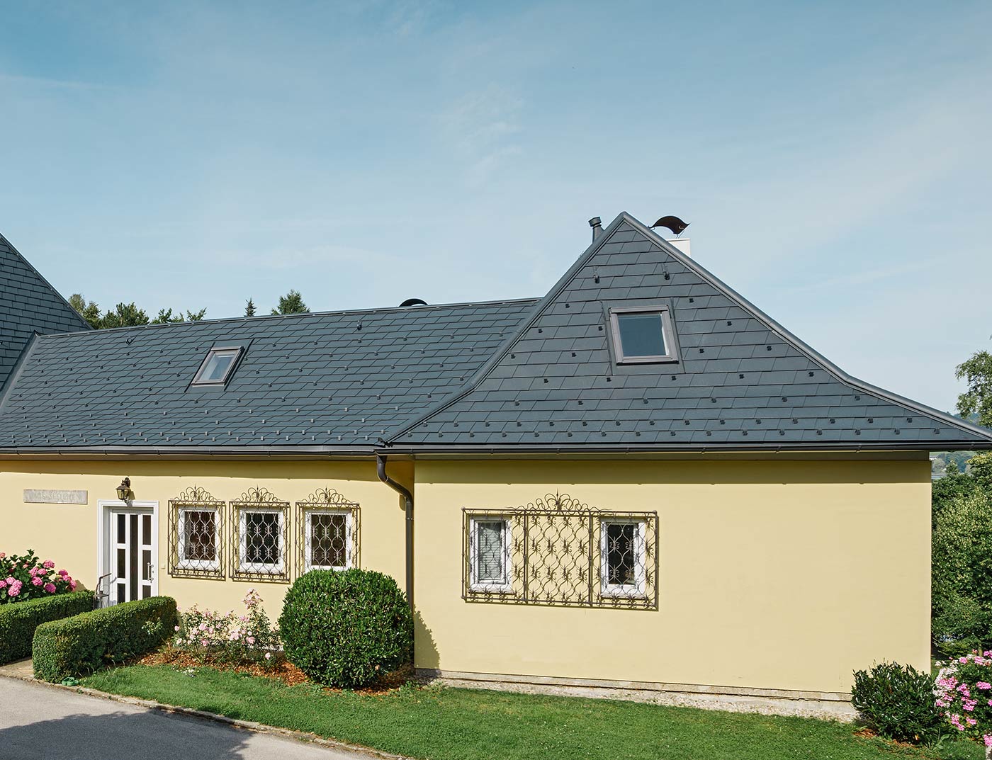 Einfamilienhaus mit Walmdach und mit gelber Putzfassade; Das Dach wurde mit der PREFA Dachschindel in Anthrazit eingedeckt.