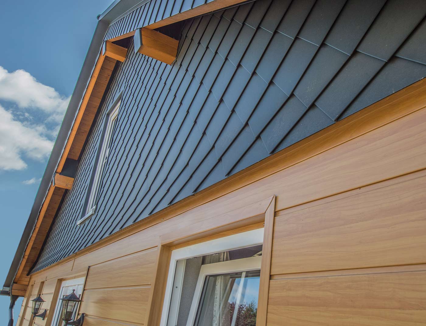 PREFA gevelvorming met de gevelbeplatingen in licht hout, alsmede een puntgevelbekleding in antraciet met de PREFA gevellosanges van 20 × 20.