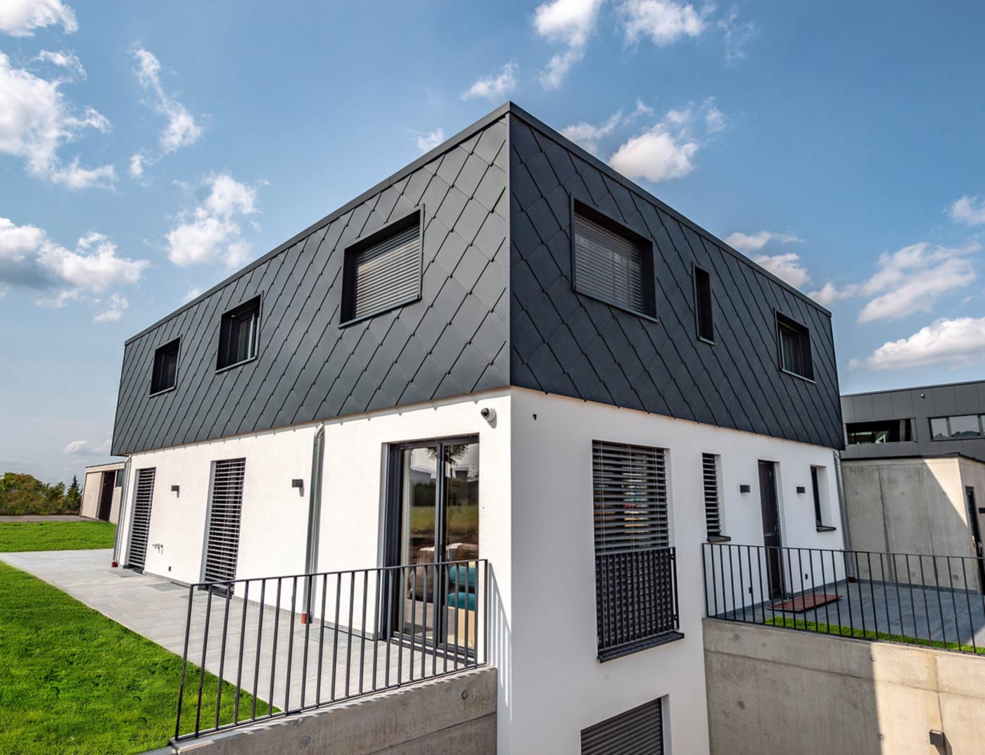 PREFA gevellosange van 44 × 44 in antraciet referentie Moderne nieuwbouw met plat dak - de gevel van de bovenverdieping is bekleed met de PREFA aluminium gevellosange van 44 × 44 in antraciet. Het onderste geveldeel is wit gestuct.